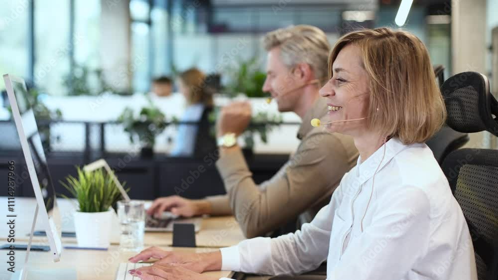 Smiling middle aged female operator call center representative customer support wearing headset working using laptop computer in office