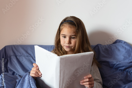 Girl with long hair reading a book sitting on the bed