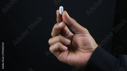 Close up male hand holding drug capsule, black background Pharmacy and medicine concept