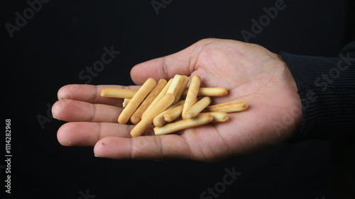 hand holding crispy straw biscuit sticks on black background.