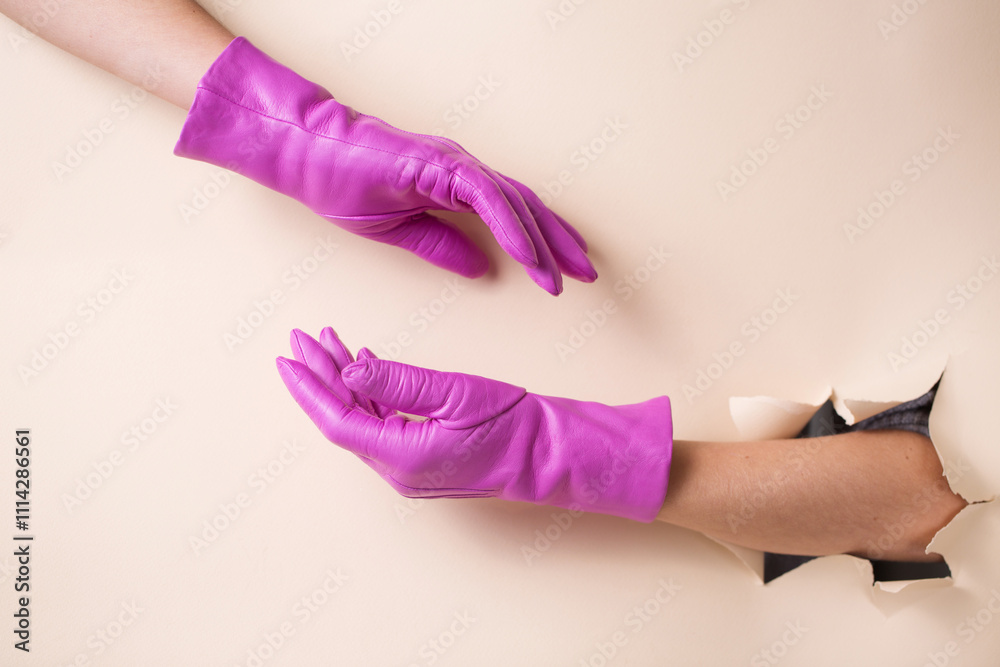 Two female hands in warm leather fuchsia gloves on a background of beige paper with a hole.