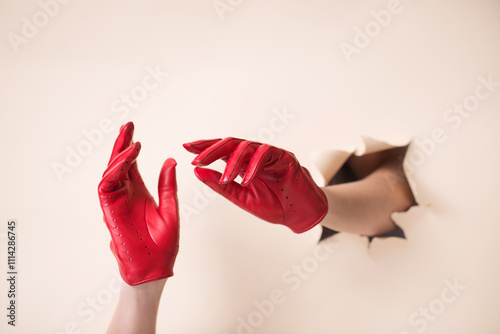 Two tender female hands in leather red gloves on a beige paper background