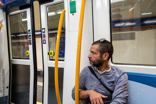 A man sits on a subway train with a yellow pole in front of him. The pole has a sign on it that says 