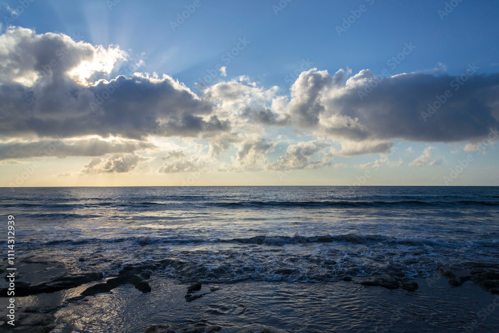 Obraz premium Breathtaking sunrise with sun hiding behind cloud, sea waves and blue sky with copy space