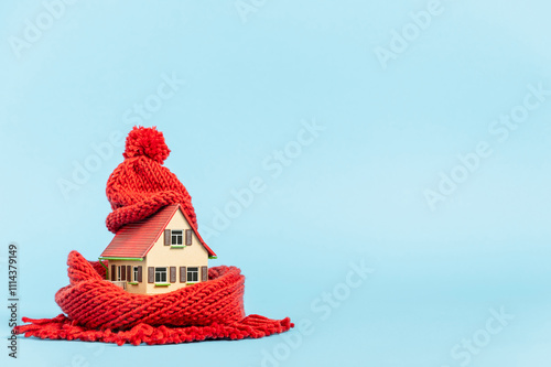 thermal insulation of buildings: tiny model house with red scarf and bobble hat, blue background