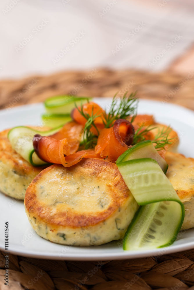 Syrniki with creamy cheese and dill, served on plate with fresh cucumber slices, thinly sliced smoked salmon, and herbs. Concept of traditional home recipes, and balanced meals. Syrniki with creamy cheese and dill, served on plate with fresh cucumber slices, thinly sliced smoked salmon, and herbs. Concept of traditional home recipes, and balanced meals.