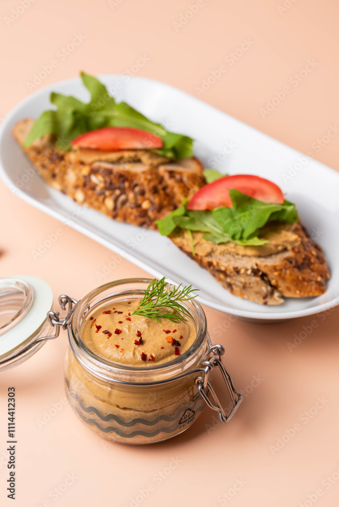 Homemade chicken liver pate in a glass jar, served with whole-grain bread topped with pate, fresh tomato slices, and arugula. A rustic and flavorful dish perfect for breakfast or a light snack. Homemade chicken liver pate in a glass jar, served with whole-grain bread topped with pate, fresh tomato slices, and arugula. A rustic and flavorful dish perfect for breakfast or a light snack.