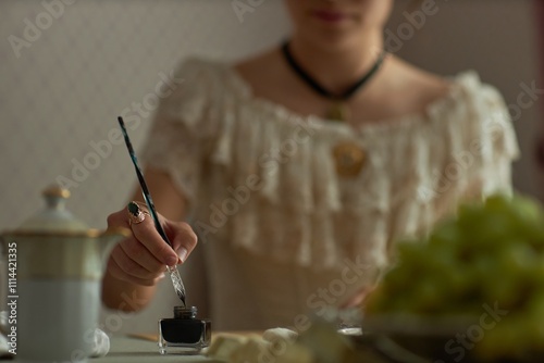 Close up of young woman dipping pen in ink while preparing to write on parchment in classic interior lit by natural light, copy space photo