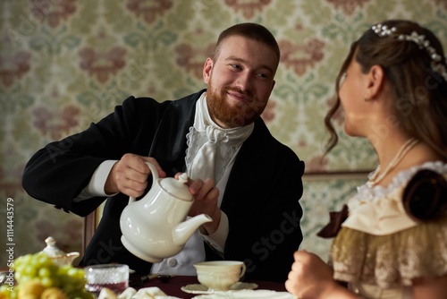 Fotografie Portrait of classic young gentleman in black tailcoat smiling while pouring tea
