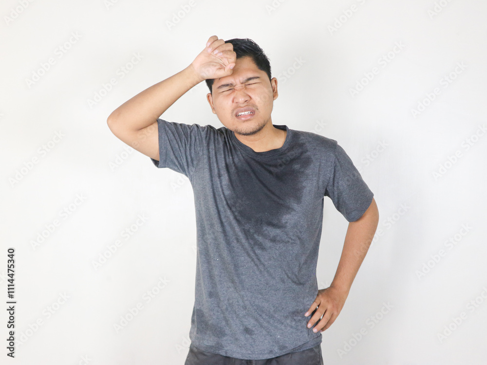 Asian man sweating while wiping sweat from his forehead with a face that looks uncomfortable Asian man sweating while wiping sweat from his forehead with a face that looks uncomfortable