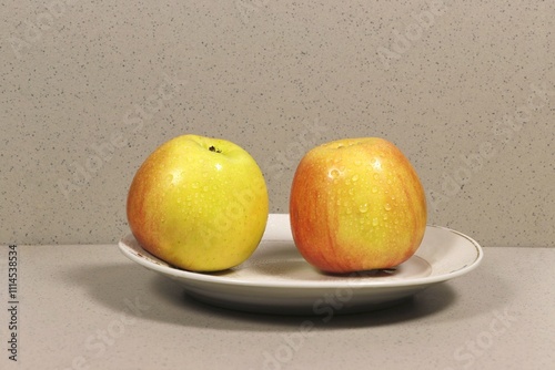 On a plate are two whole apples with drops of moisture.