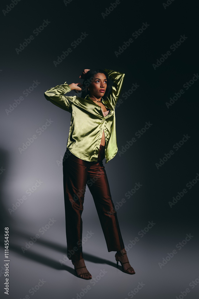 Fototapeta premium An attractive young African American woman showcases style in a green silk shirt while posing.