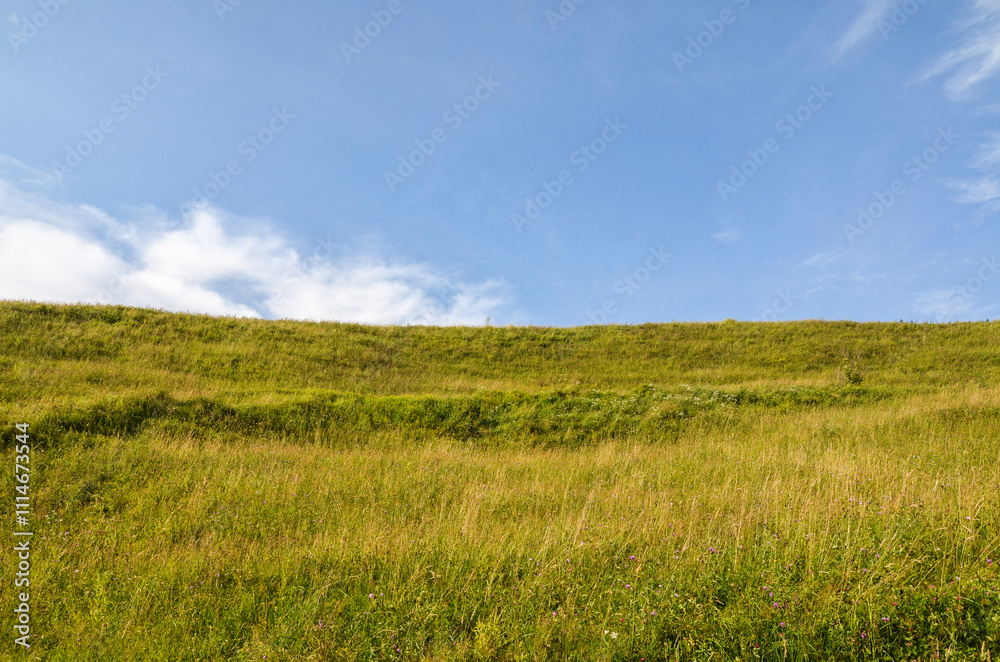 Peaceful view of a green grassy hill under a vast clear blue sky, evoking calmness and freedom. Ideal for nature, tranquility, and relaxation themes Peaceful view of a green grassy hill under a vast clear blue sky, evoking calmness and freedom. Ideal for nature, tranquility, and relaxation themes