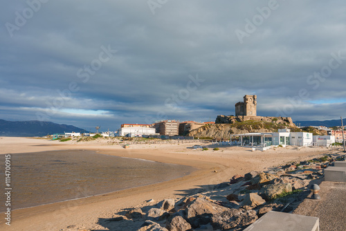 Tarifa's Guzman Castle stands on a rocky hill, overlooking the sandy beach and Atlantic Ocean. The overcast sky adds drama to the historic landscape. photo