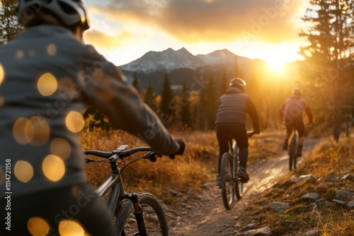 Three cyclists ride through a picturesque mountain trail, their paths illuminated by the warm glow of the setting sun against the stunning backdrop of the mountains. photo