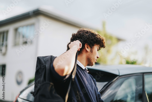 A parent is seen dropping off their teenage son at school, car parked nearby. The morning setting and casual attire indicate a typical school day routine. photo