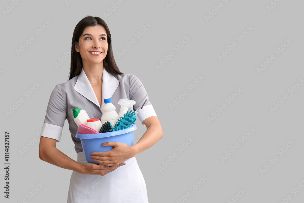 Young chambermaid with cleaning supplies on light background Young chambermaid with cleaning supplies on light background