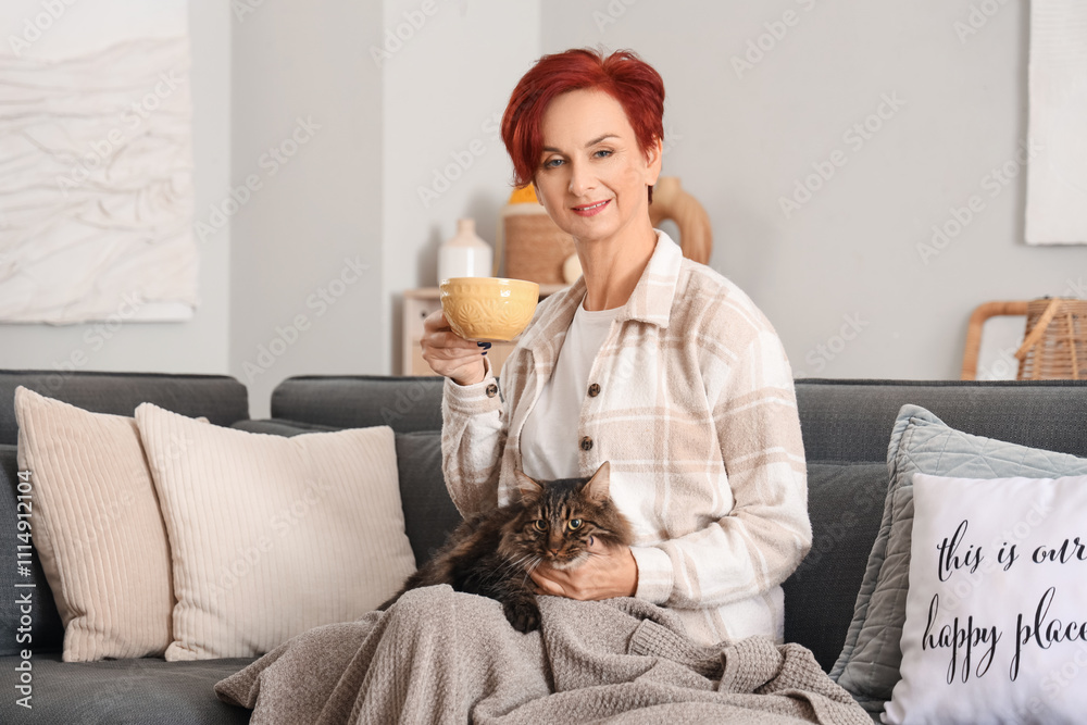 Obraz premium Beautiful happy mature woman with cute cat and cup of tea sitting on sofa at home