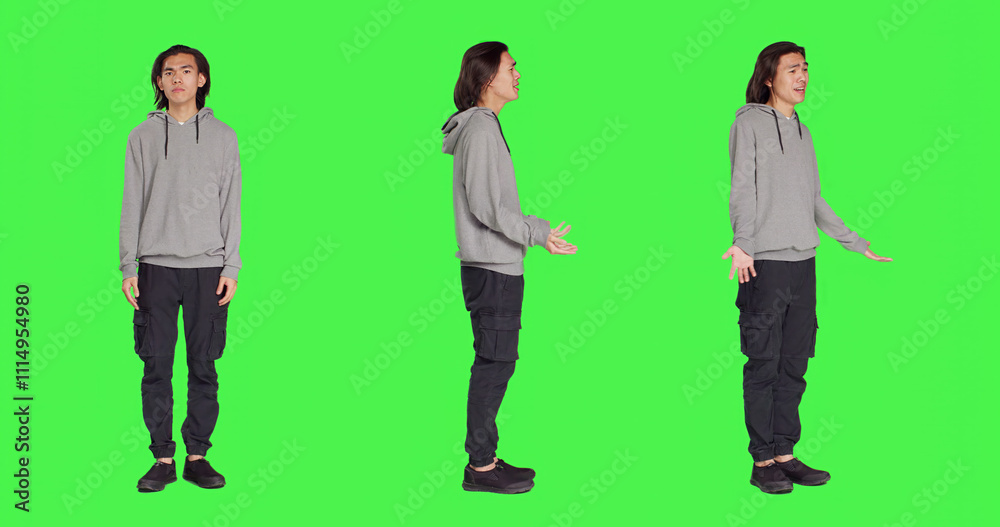 Obraz premium Young unsure guy shrugging on camera, doing i dont know sign after hearing question. Model feeling clueless and uncertain over full body greenscreen backdropground, doubtful person.