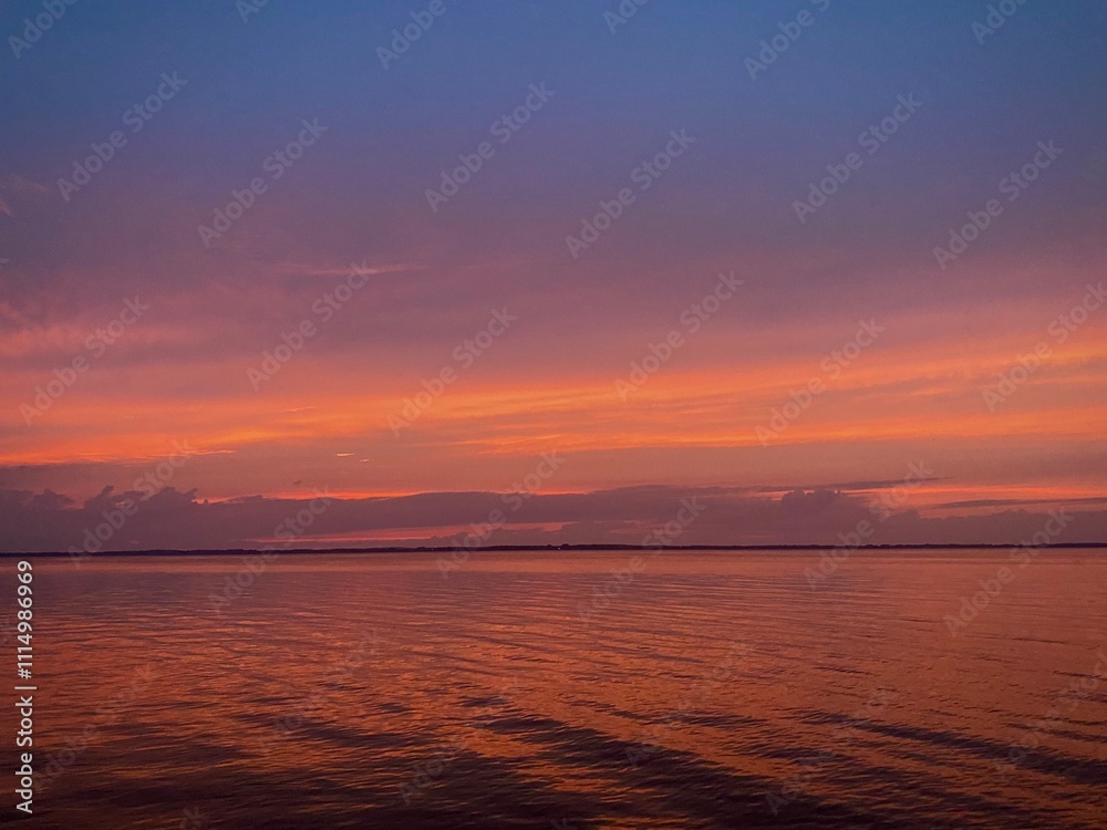 Obraz premium purple and orange sunset with clouds over the water on lake with waves
