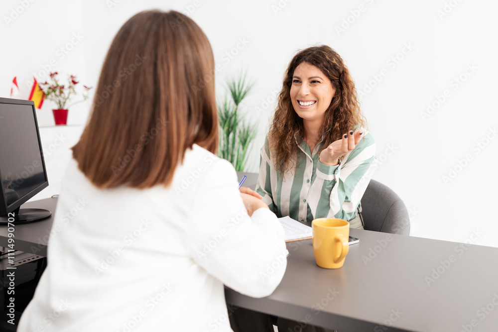 Two Caucasian women engage in a professional discussion in a bright office setting. One woman speaks animatedly while the other listens attentively, fostering a collaborative atmosphere. Two Caucasian women engage in a professional discussion in a bright office setting. One woman speaks animatedly while the other listens attentively, fostering a collaborative atmosphere.