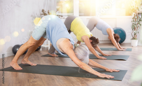 Calm old woman practicing downward dog pose of yoga on black rug during fitness classes photo