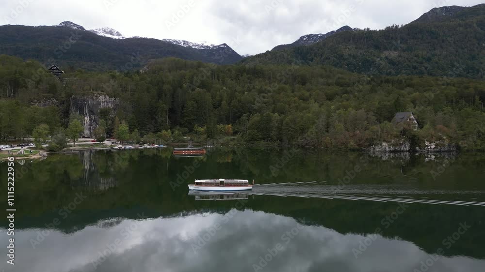 A peaceful boat gliding across Lake Bohinj with forested hills and alpine scenery. A peaceful boat gliding across Lake Bohinj with forested hills and alpine scenery.