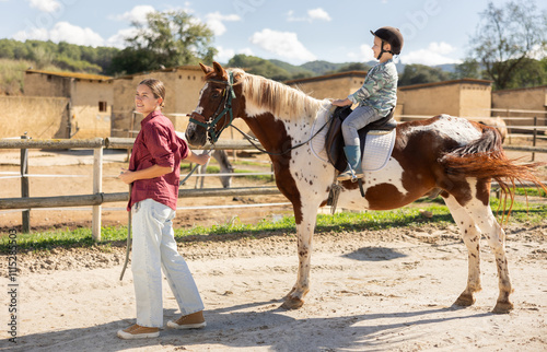 Young woman leads horse on leash with boy rider in paddock photo