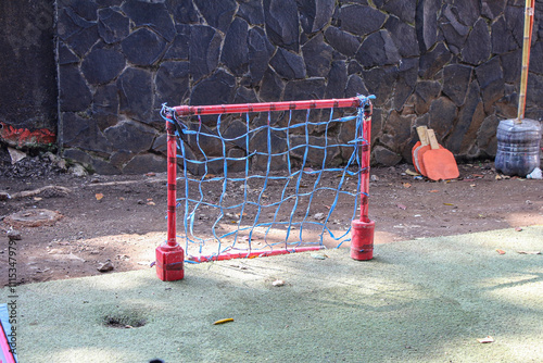 Φωτογραφία A simple, hand-made soccer goal made of red poles and blue netting sits against a stone wall