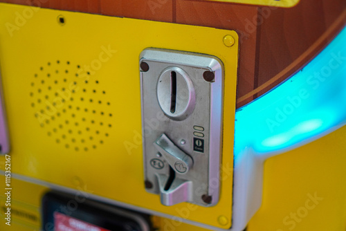 A detailed close up shot of a yellow arcade game machine's coin slot, highlighting the texture and design. The blue light adds a vibrant touch.