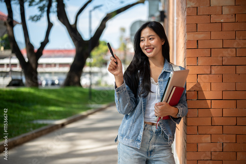 A female student stands leaning against a brick building wall, smiling and looking to the side.