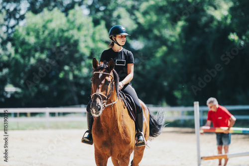 Fototapet A young equestrian wearing a helmet riding a horse in an outdoor arena on a sunny day