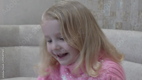 little girl smiling on the couch, happy cheerful mood of a girl in a pink sweater on Christmas day