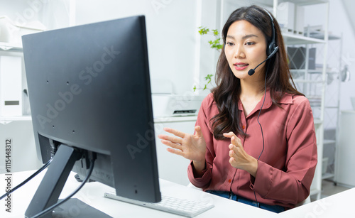 Confident Asian female call center agent with headset talking to client support for customer care in office. Asian woman telemarketing agent working on computer for consulting, customer support.