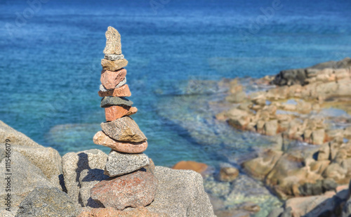red and grey pebbles stacked on the rock in front of beautiful sea of Sardini...