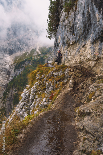 A person is standing on a rocky path with a view of the mountains. The person is wearing a red shirt and he is enjoying the scenery photo