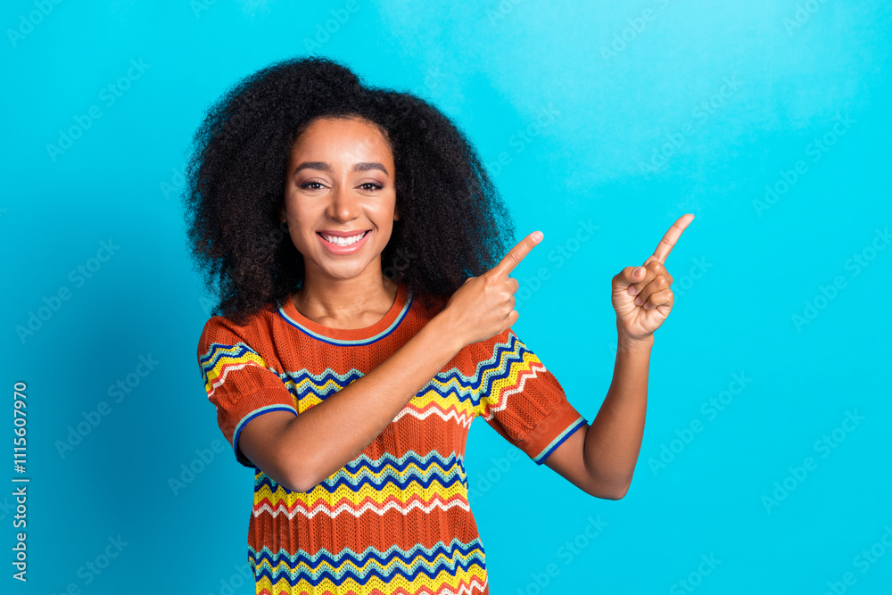 Charming young woman in colorful t-shirt pointing with both hands on vibrant blue background Charming young woman in colorful t-shirt pointing with both hands on vibrant blue background