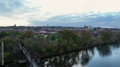 Drone rising shot of suspension Bridge over river in Danville City at sunset. Autumn trees in color. Red brick Buildings and homes with clouds at sky. Virginia, USA. photo