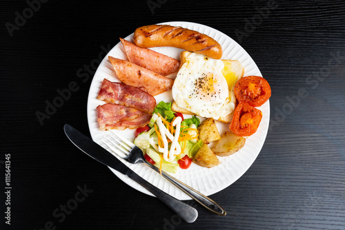 Top view American breakfast set with eggs,bacon,toast, potatoes, tomatoes, mayonnaise sauce and sausage on black background.