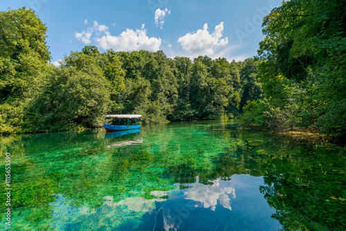 Navigating with a wooden oar on crystal clear waters of Black Drin springs in lake Ohrid, North Macedonia, surrounded by lush greenery and a lakeside restaurant on a sunny summer day photo