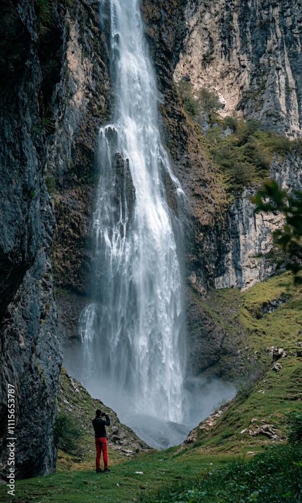Obraz premium A photographer capturing stunning shots beneath a majestic waterfall, with water cascading around them in a dramatic display of nature’s power. The photographer is focused on their craft, immersed in