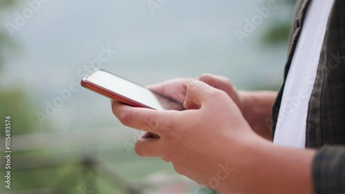 4K Closeup shot of hands of an Indian man using mobile phone while standing outdoors. Man types and swipes on his mobile phone. Smartphone addiction background with copy space for text.