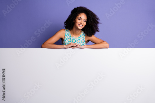 Vibrant young woman with afro hair posing against a purple background holding a blank white sign for promotional or advertising purposes photo