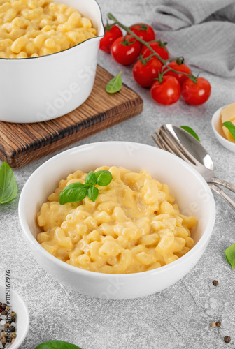 Mac and cheese in a white bowl with fresh basil on top on a gray concrete background. American cuisine, comfort food. Copy space.