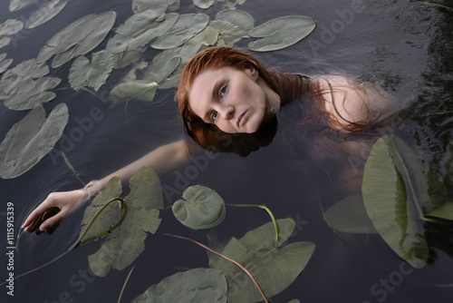 A red-haired girl in the river among the leaves of water lilies photo