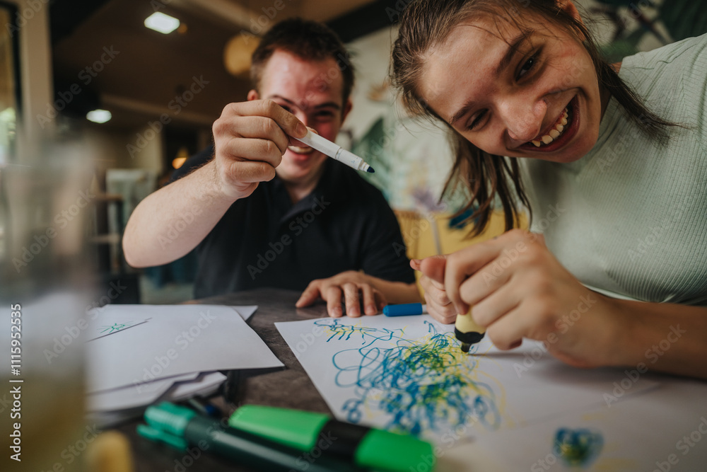 Fototapeta premium Happy young friends, one with Down syndrome and one in a wheelchair, joyfully engaged in drawing and painting. Their creativity and friendship highlight inclusivity and fun.