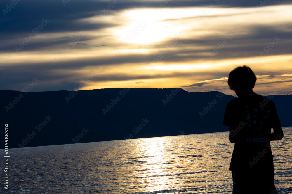Fototapeta premium a person standing on the shore of a lake at sunset