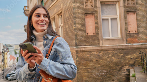 Foto Woman smiling while holding her phone, with colorful buildings and sunshine all around