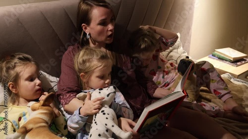 Mom reads fairy tales to three little triplet daughters lying in pajamas 