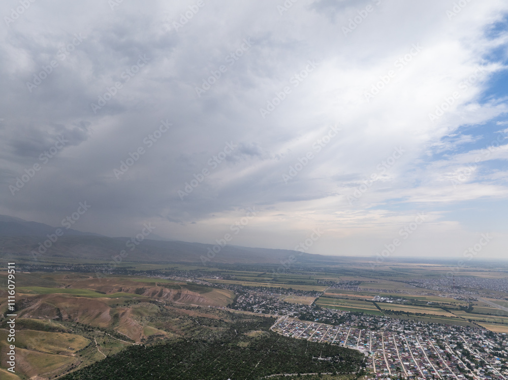 Drone view of the mountains, fields and villages in cloudy weather. Large dark clouds in the sky. Green and yellow grass on the hills. Drone view of the mountains, fields and villages in cloudy weather. Large dark clouds in the sky. Green and yellow grass on the hills.